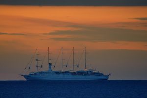 Le voilier Club Med 2 de profil sur la mer au crépuscule, ses cinq mâts se découpant sur un ciel orangé