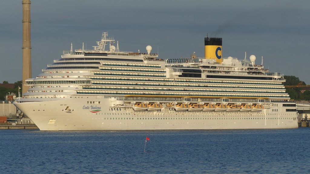Le paquebot Costa Diadema, coque blanche et cheminée jaune au logo C de Costa, naviguant de profil en quittant le port de Kiel