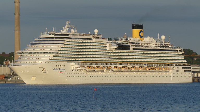 Le paquebot Costa Diadema, coque blanche et cheminée jaune au logo C de Costa, naviguant de profil en quittant le port de Kiel