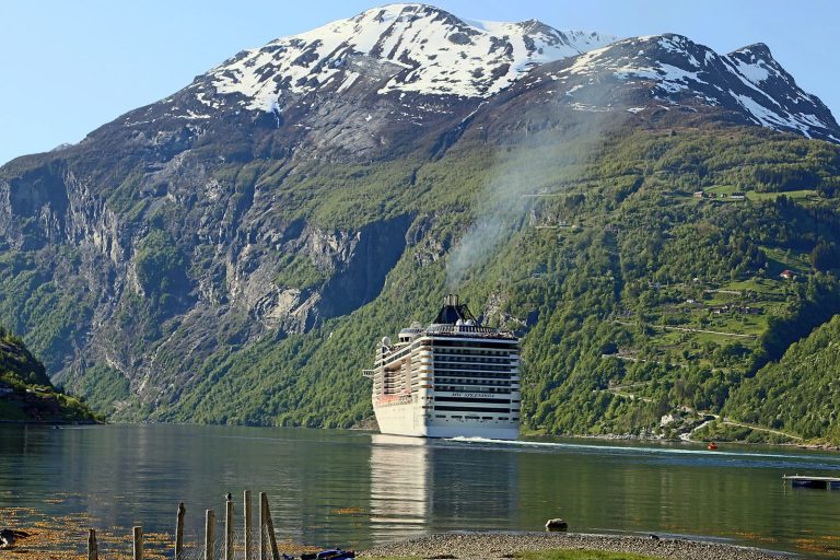 Le paquebot blanc MSC Splendida navigue sur les eaux calmes du Geirangerfjord, au pied de montagnes vertes aux sommets enneigés