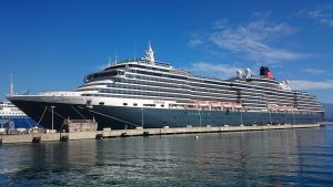Le paquebot Queen Victoria de Cunard, coque bleu nuit et cheminée rouge et noire, amarré à un quai du port d'Ajaccio sous un ciel bleu