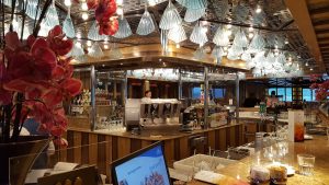 Le Palatino Grand Bar du Costa Favolosa : comptoir en bois, machine à expresso, bouteilles d'alcool et lustres en verre en forme de coquillage