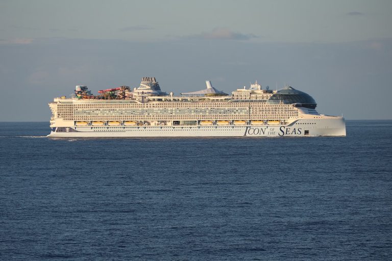 Le paquebot Icon of the Seas de Royal Caribbean naviguant de profil en pleine mer, avec le parc aquatique à l'arrière et le dôme vitré à l'avant