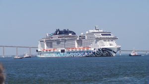 Le paquebot MSC Euribia escorté par des remorqueurs dans l'estuaire de la Loire, devant le pont de Saint-Nazaire, avec sa coque décorée d'une fresque bleue et de l'inscription #savethesea