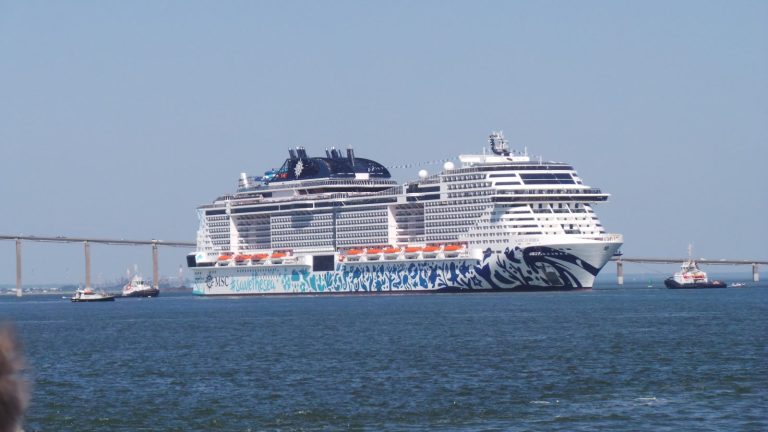 Le paquebot MSC Euribia escorté par des remorqueurs dans l'estuaire de la Loire, devant le pont de Saint-Nazaire, avec sa coque décorée d'une fresque bleue et de l'inscription #savethesea