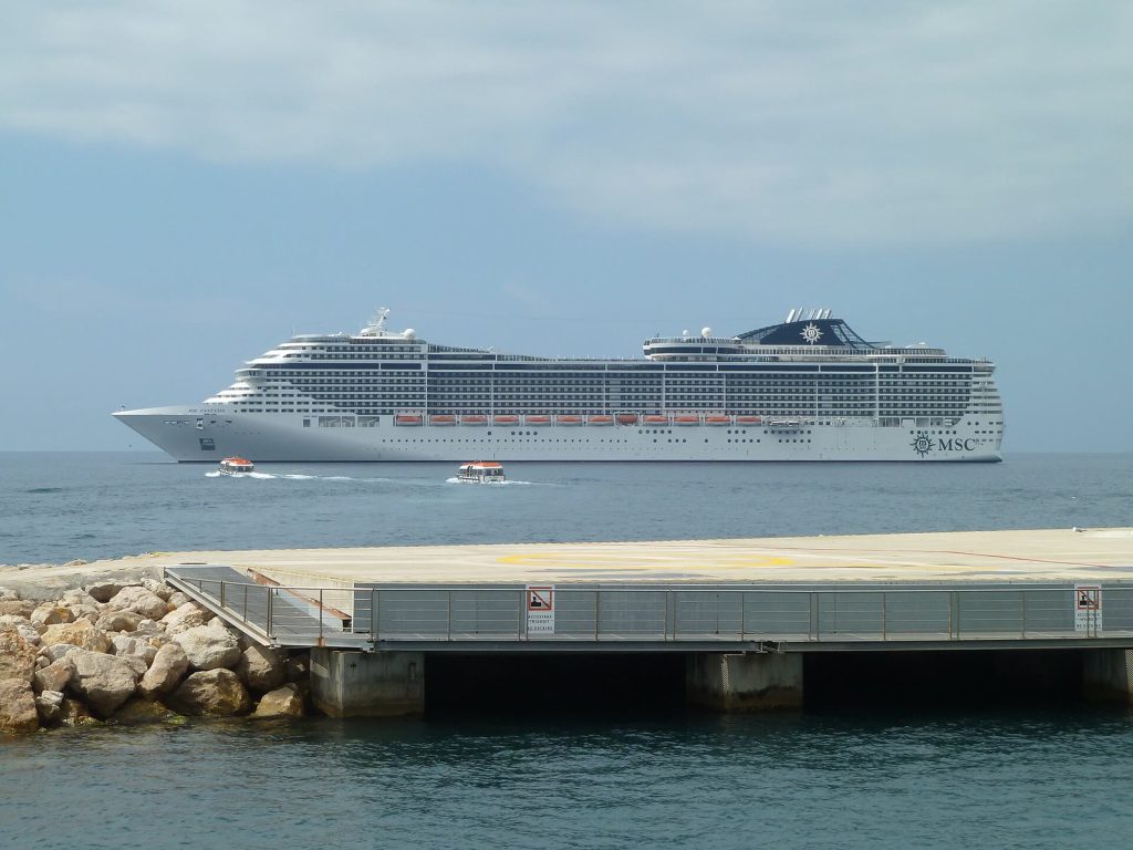 Le paquebot MSC Fantasia vu de profil au mouillage dans la baie de Cannes, avec deux petites navettes sur l'eau et une jetée au premier plan