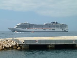 Le paquebot MSC Fantasia vu de profil au mouillage dans la baie de Cannes, avec deux petites navettes sur l'eau et une jetée au premier plan