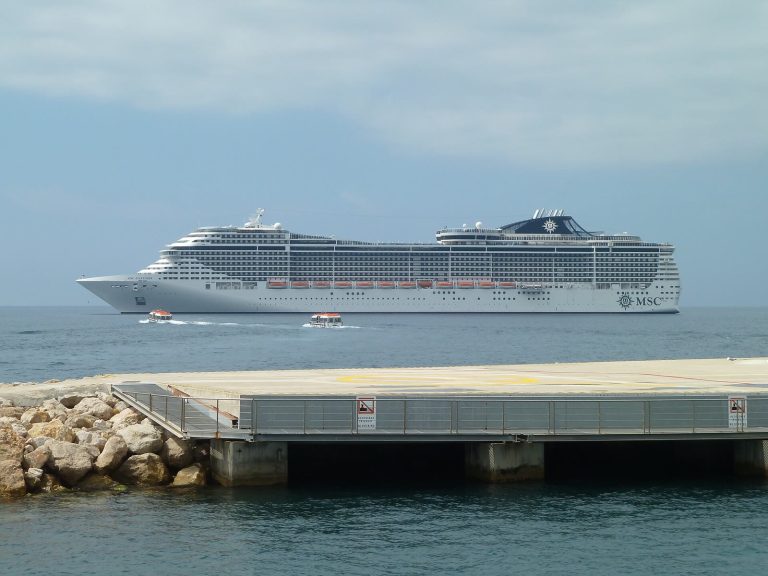 Le paquebot MSC Fantasia vu de profil au mouillage dans la baie de Cannes, avec deux petites navettes sur l'eau et une jetée au premier plan