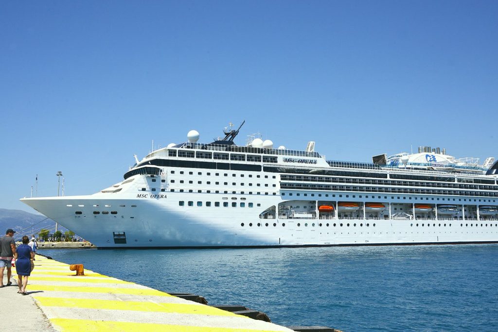 Le paquebot MSC Opera, coque blanche et cheminée sombre, amarré le long d'un quai peint en jaune, avec des promeneurs au premier plan