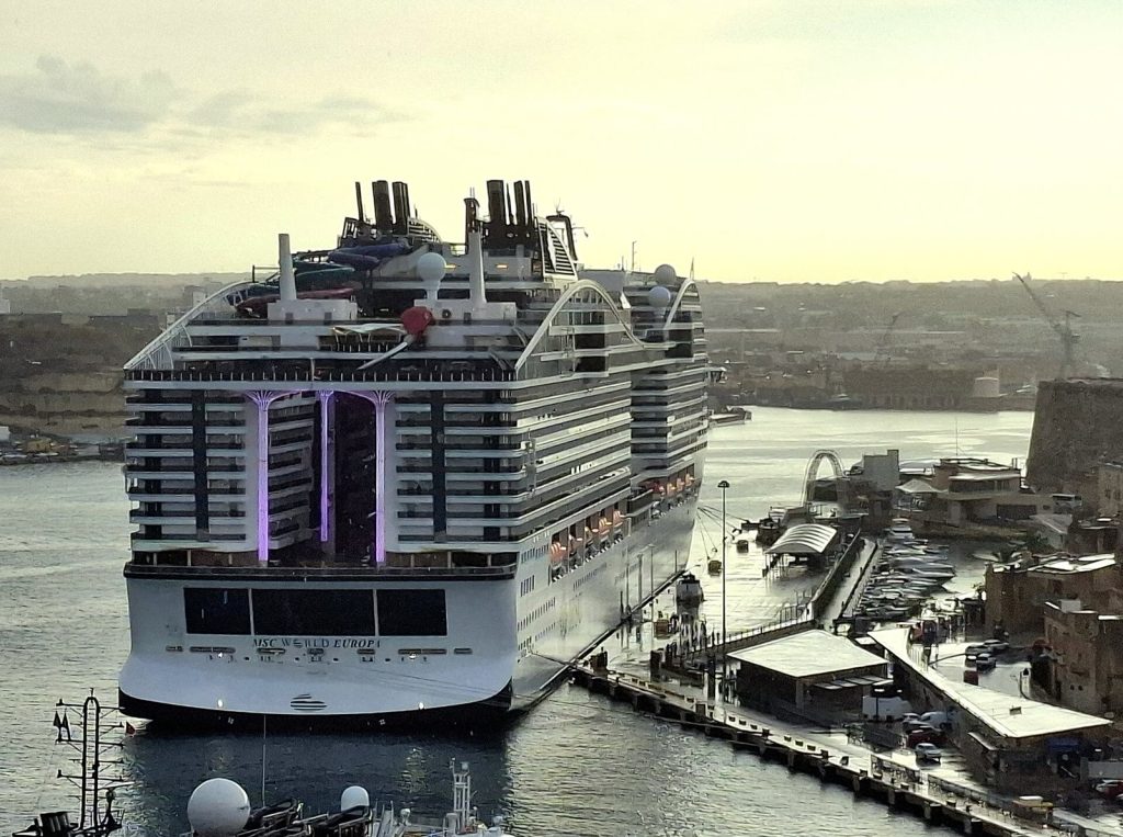Le paquebot MSC World Europa vu de l'arrière, amarré dans le port de La Valette, avec la World Promenade éclairée au centre de la poupe et les toboggans sur le pont supérieur