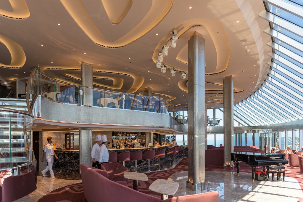 Le Top Sail Lounge du MSC Yacht Club à bord de MSC Seaside : salon sur deux niveaux avec fauteuils roses, piano à queue, bar et grande verrière ouverte sur la mer