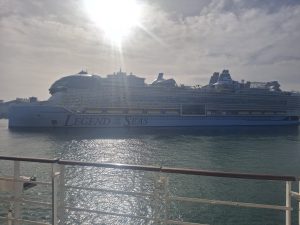 Le paquebot Legend of the Seas de Royal Caribbean vu de profil depuis le pont d'un autre navire, dans le port de Barcelone, avec son dôme vitré à l'avant et ses toboggans à l'arrière