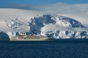 Le navire Le Lyrial de la compagnie Ponant naviguant de profil devant un glacier enneigé en Antarctique