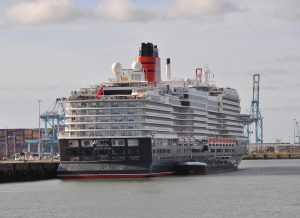 Le paquebot Queen Anne de Cunard, coque noire à liseré rouge et cheminée rouge et noire, amarré à un quai du port de Zeebrugge, vu par l'arrière avec son nom sur la poupe
