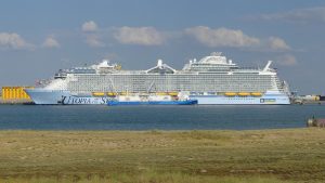 Le paquebot Utopia of the Seas de Royal Caribbean à quai à La Rochelle-La Pallice, vu de profil depuis la côte, avec un petit navire bleu le long de sa coque