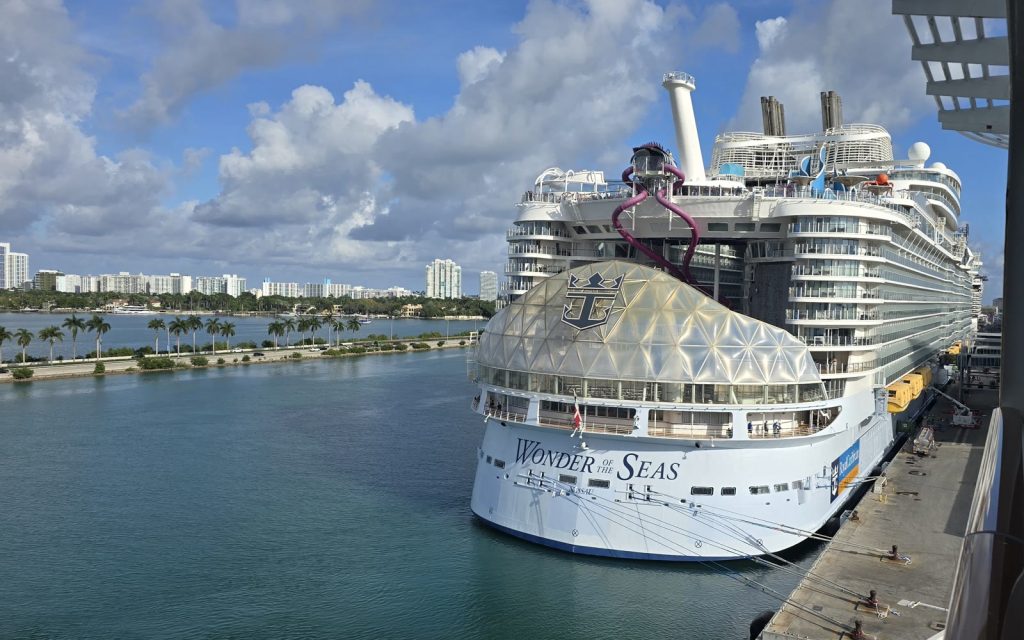Le paquebot Wonder of the Seas de Royal Caribbean à quai à Miami, son nom inscrit en grand sur la coque, avec un toboggan violet sur les ponts supérieurs et des palmiers en arrière-plan