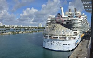Le paquebot Wonder of the Seas de Royal Caribbean à quai à Miami, son nom inscrit en grand sur la coque, avec un toboggan violet sur les ponts supérieurs et des palmiers en arrière-plan