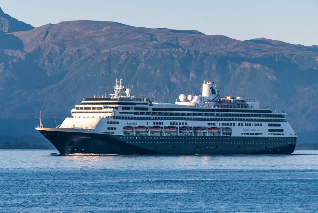 Le paquebot Zaandam de Holland America Line, coque bleu nuit et superstructure blanche, naviguant de profil devant des montagnes en Alaska