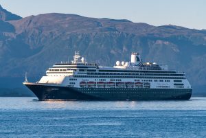 Le paquebot Zaandam de Holland America Line, coque bleu nuit et superstructure blanche, naviguant de profil devant des montagnes en Alaska
